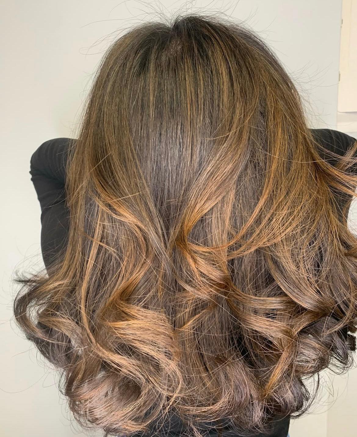 Back view of medium brunette hair with caramel balayage and curled ends