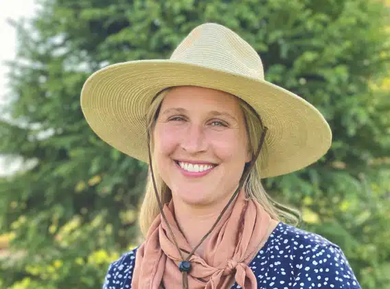 Kristin Meek, smiling in a wide-brim straw hat outdoors among trees
