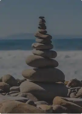Stacked zen stones on a rocky beach with ocean and mountains behind