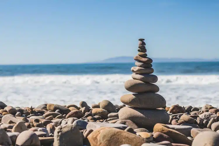 Balanced zen-stone cairn on a rocky ocean beach beneath a clear blue sky