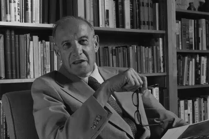 Black-and-white portrait of Peter Drucker seated before a bookshelf