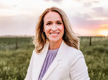Kristin Meek, WYLD Guide, in a white blazer outdoors against a sunset field sky