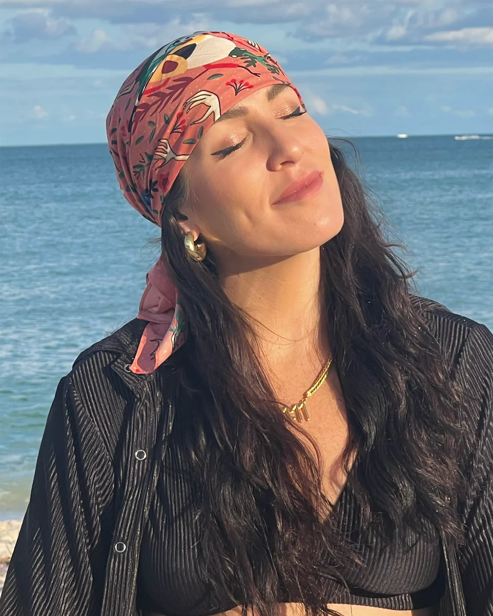 Lana Rose with eyes closed and a floral headscarf, facing the sunlight at the beach