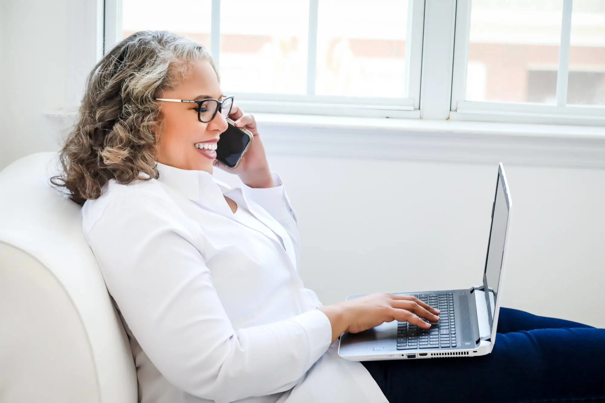 Yvonne Victor smiling while talking on the phone and working on her laptop