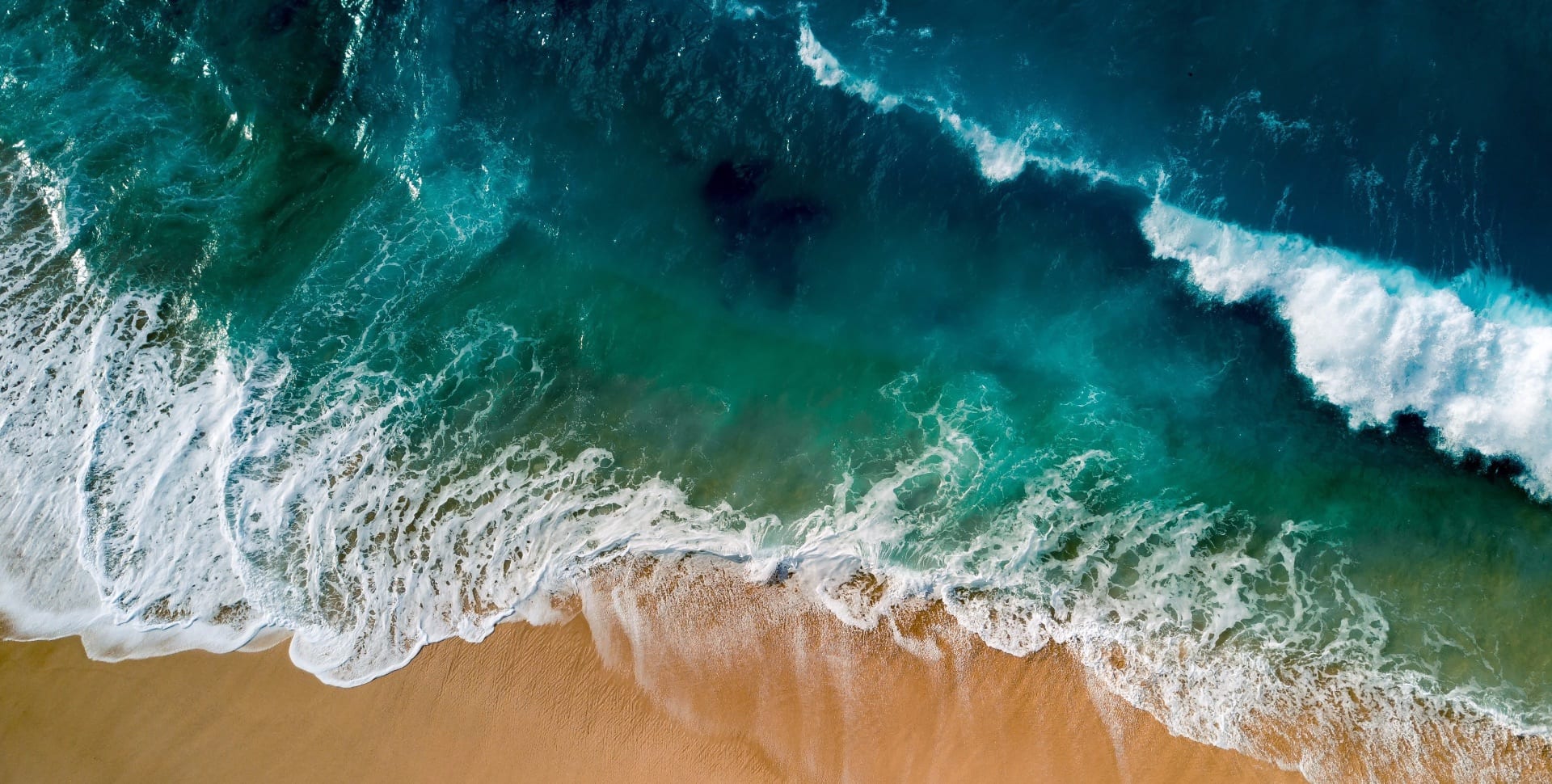 Aerial drone shot of turquoise ocean waves breaking on a sandy beach shoreline