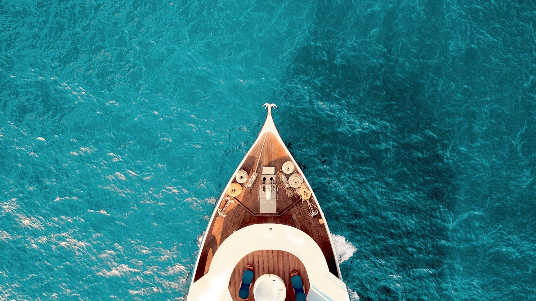 Aerial top-down view of a luxury yacht bow sailing through deep turquoise water